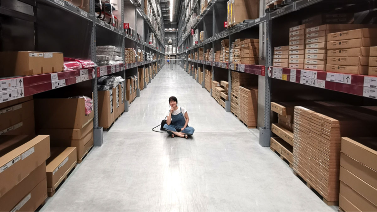 Woman sits cross-legged in a warehouse aisle