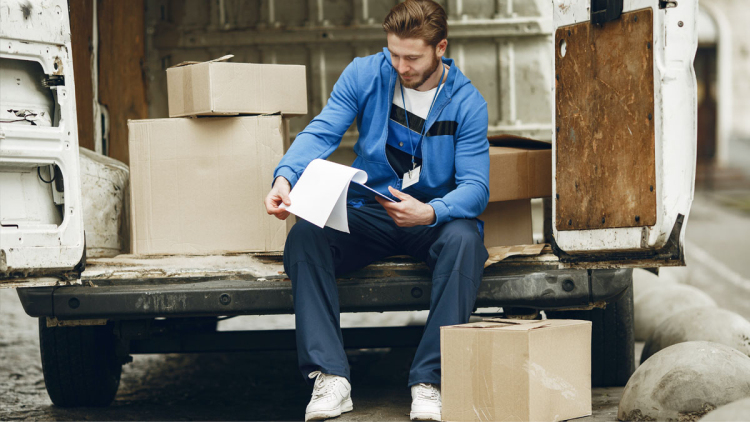 Man in blue hoodie looks at manifest sitting in the back of a delivery van