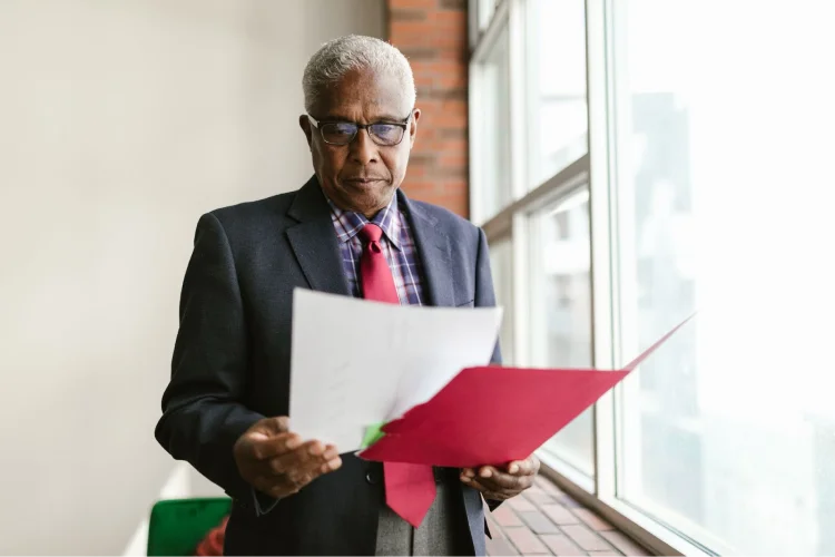A man in a suit looks over documents in a red folder