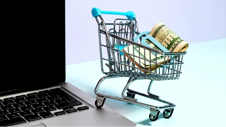 Mini shopping cart with a full money clip perched on an apple macbook laptop