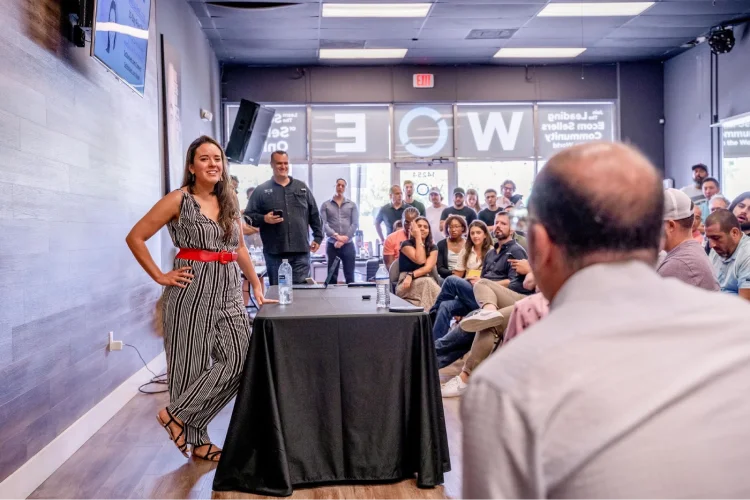 Person leaning on table and speaking with an event crowd.