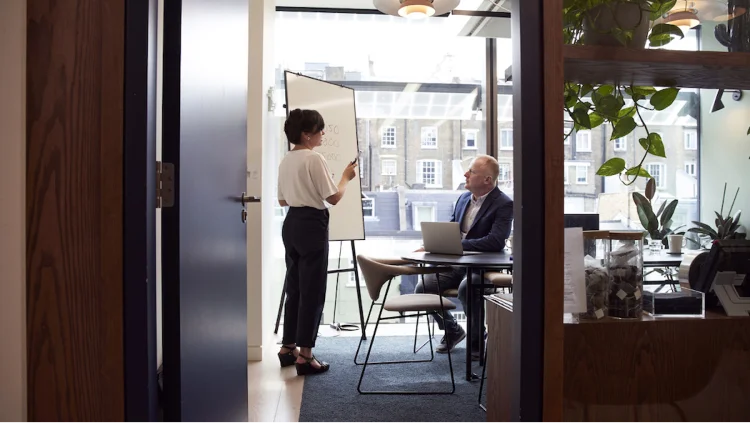 Business woman presents marketing report on a whiteboard in front of a colleague