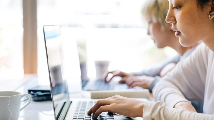 Young professional types on her laptop next to a colleague
