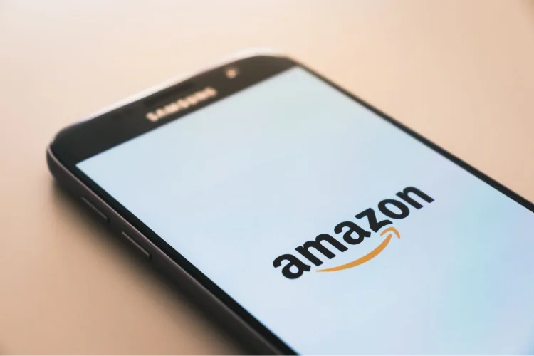 A smartphone sits on a surface with the Amazon app opening.